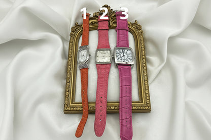 Three watches with different colored straps (pink, red, and orange) on a white background.