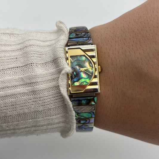 Close-up of a wristwatch with abalone shell strap on a person's wrist.